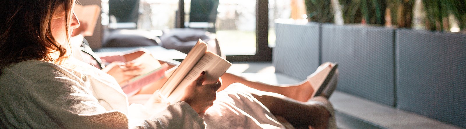 Frau auf Liege im Bademantel liest ein Buch