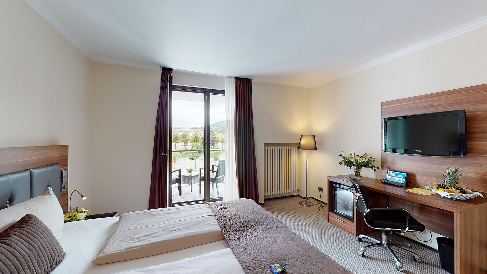 Innansicht Comfortzimmer mit Doppelbett, Schreibtisch und Glastür zum Balkon